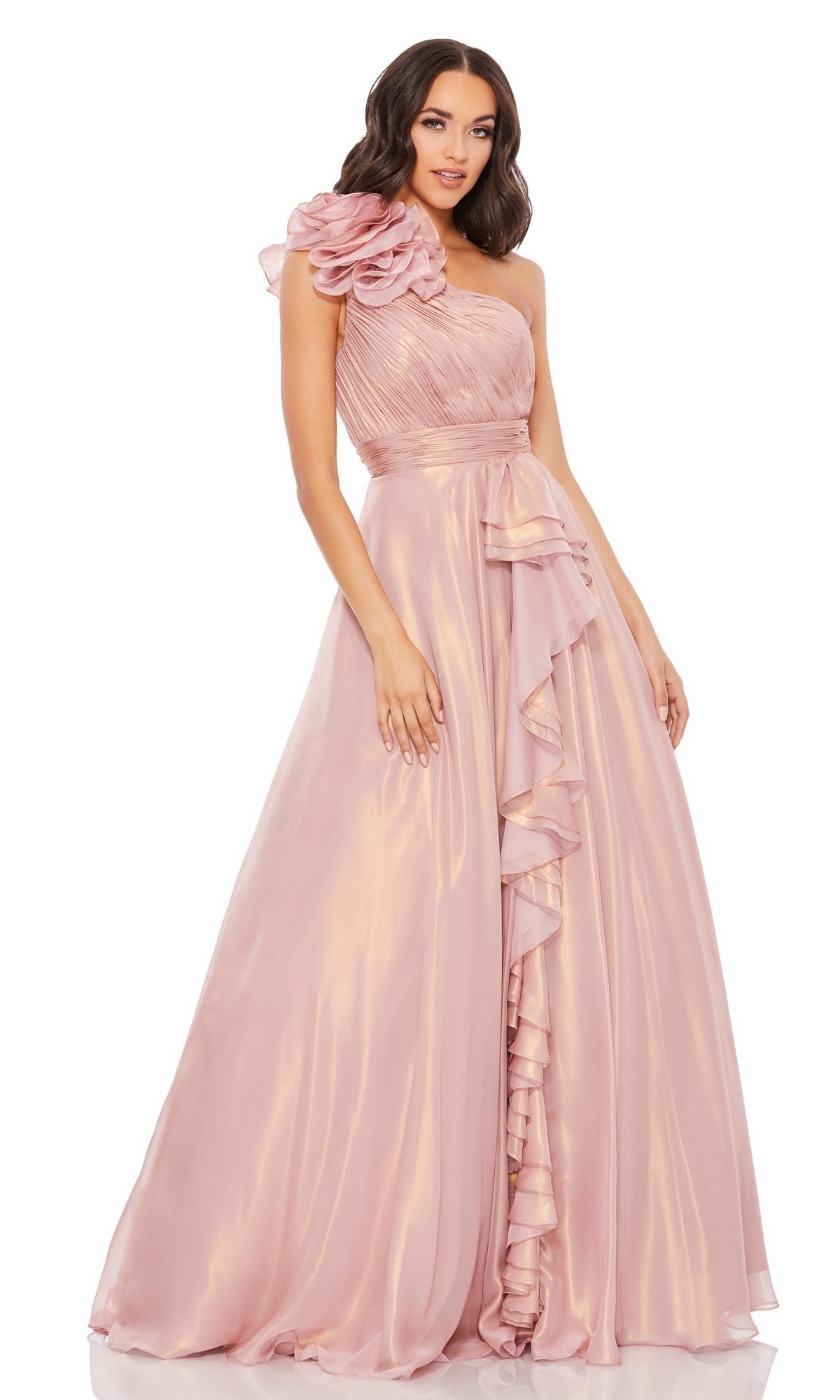 A woman wearing the Mac Duggal 49252 long rose gold formal dress, featuring a one-shoulder design with floral detail on the shoulder and elegant ruffled accents cascading down the skirt.